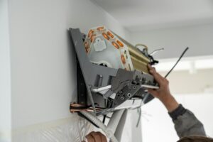 Hands of man technician in uniform check installing air conditioner in modern apartment.