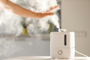 Man holds hand over steam aroma oil diffuser on table at home, steam from air humidifier